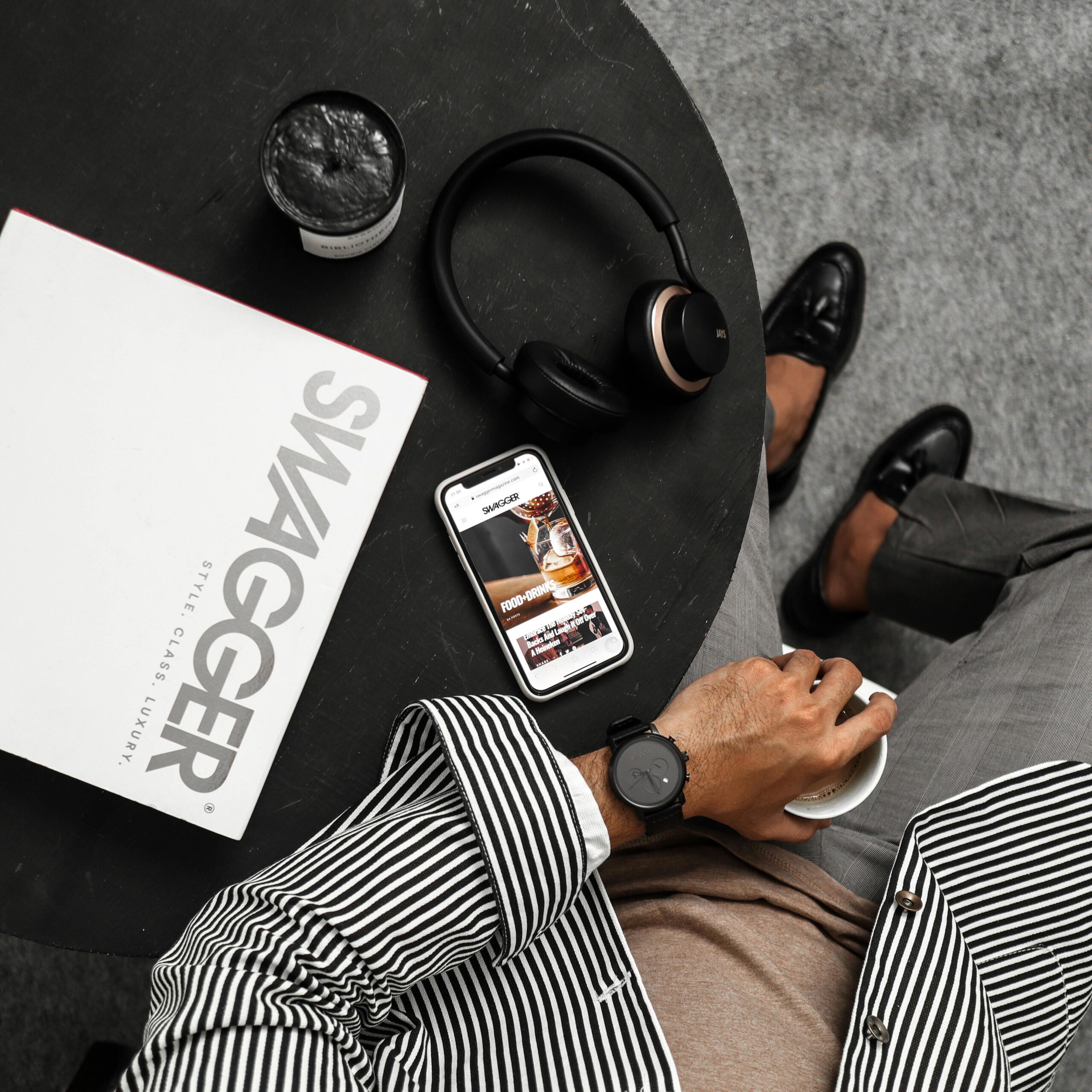 Top view of a stylish man with headphones, smartphone, and swagger magazine on a round table.